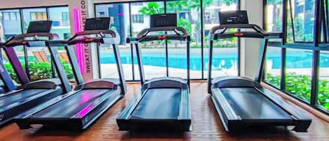 A gym with treadmills aligned in a row, large windows, and a view of a pool outside.