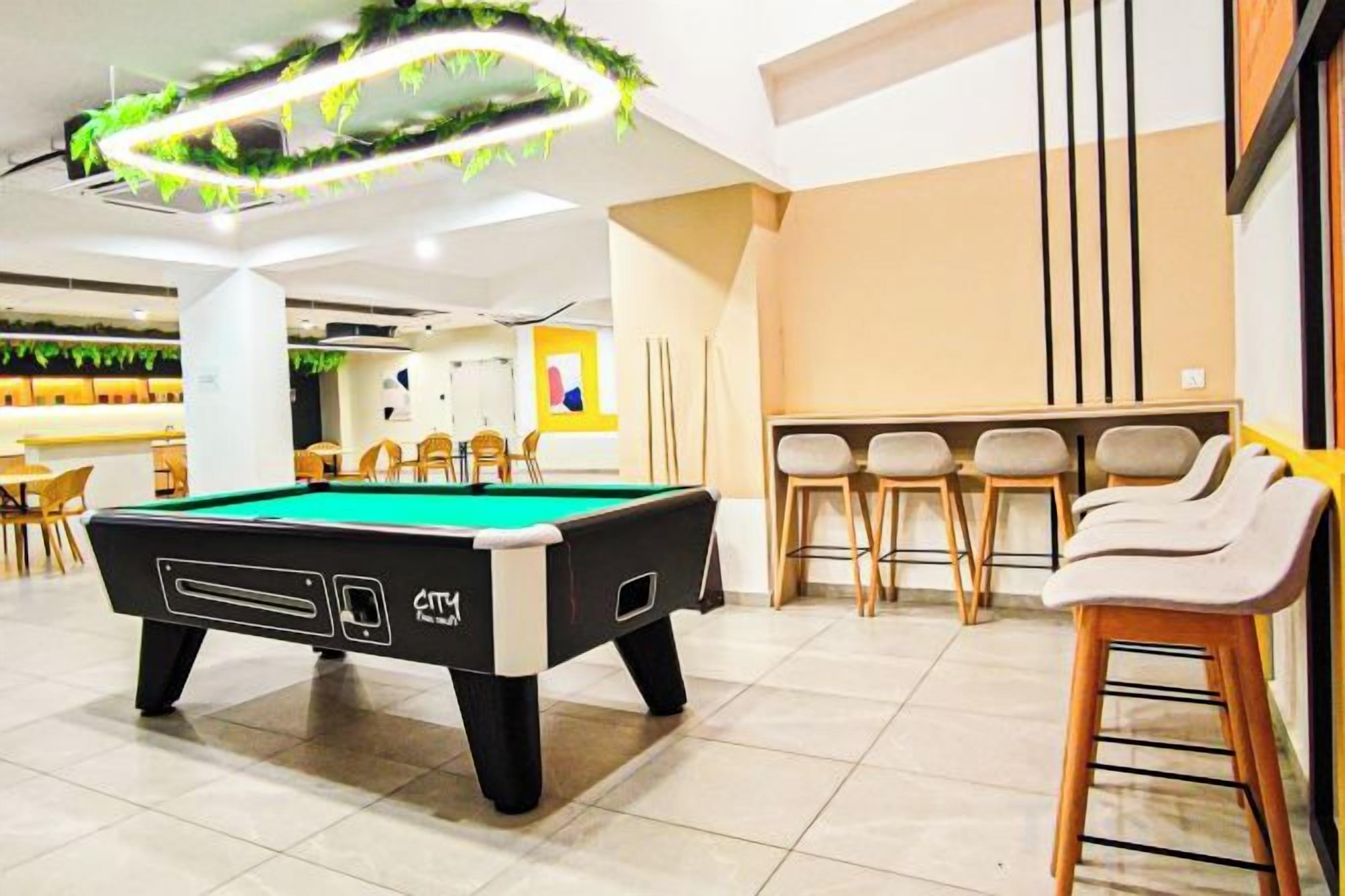 A pool table in a room with bar stools and a bar area.
