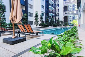 A swimming pool area with lounge chairs and umbrellas, surrounded by greenery and modern buildings. - Fluffy Stay at Huni Setia Alam by HCK (Shah Alam)