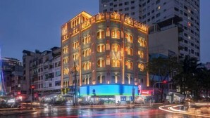 A multi-story hotel with a prominent 'M' logo, surrounded by urban buildings and a wet street reflecting city lights. - Express by M Village Pham Ngu Lao, a brand of Modern Village Lifestyle (Ho Chi Minh City)