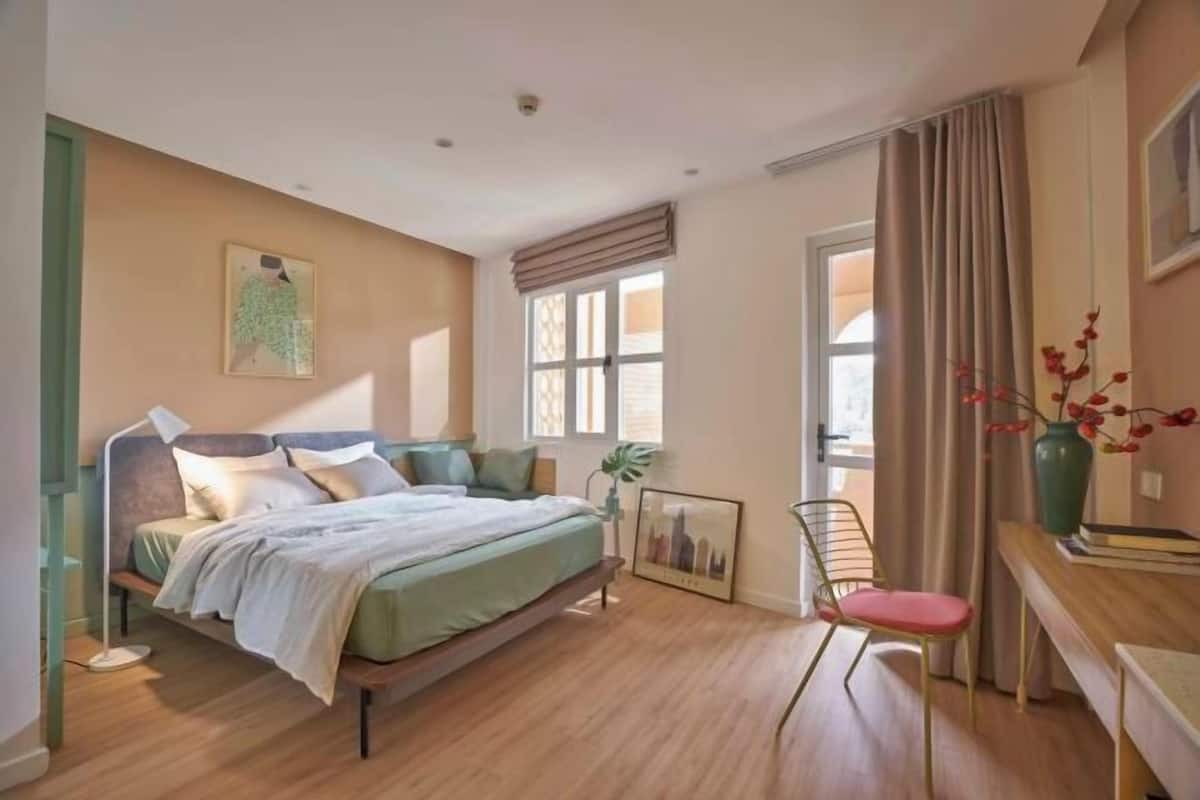 Une chambre à coucher avec un lit, une table de chevet, une chaise et une fenêtre avec des rideaux.