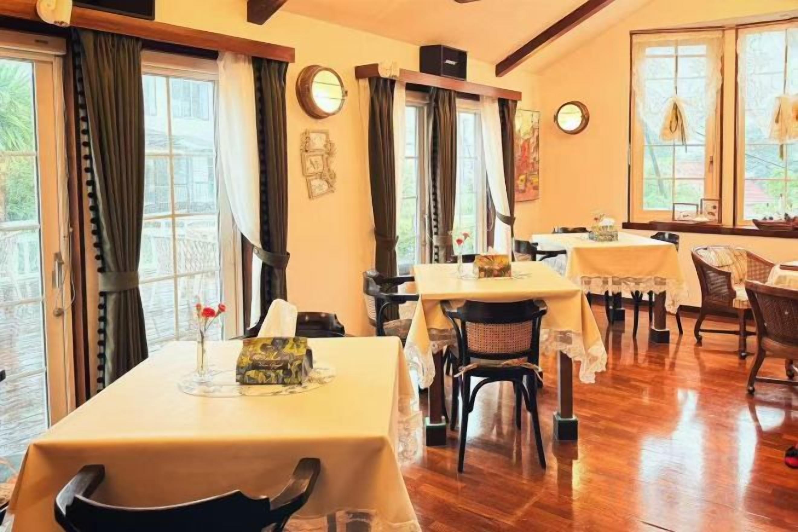 Un comedor con mesas y sillas, un reloj en la pared y un ventanal con cortinas.