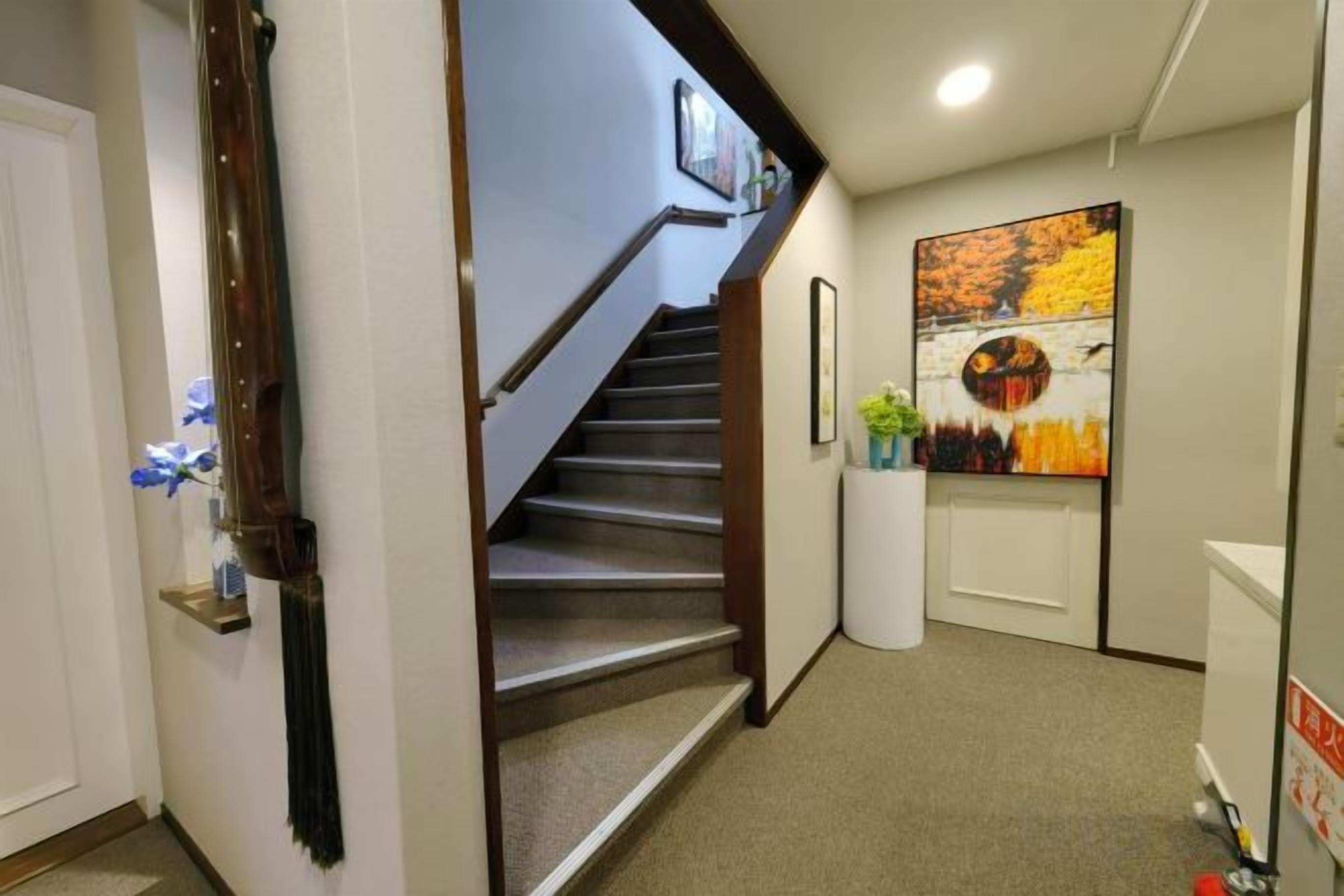 Un pasillo con piso alfombrado, una escalera de madera, una puerta blanca y un cuadro colgado en la pared.