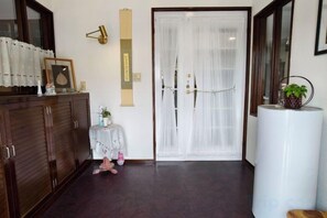 Una stanza con un armadio in legno, un tavolino con una pianta, una porta bianca con tende e un ampio pilastro bianco.
