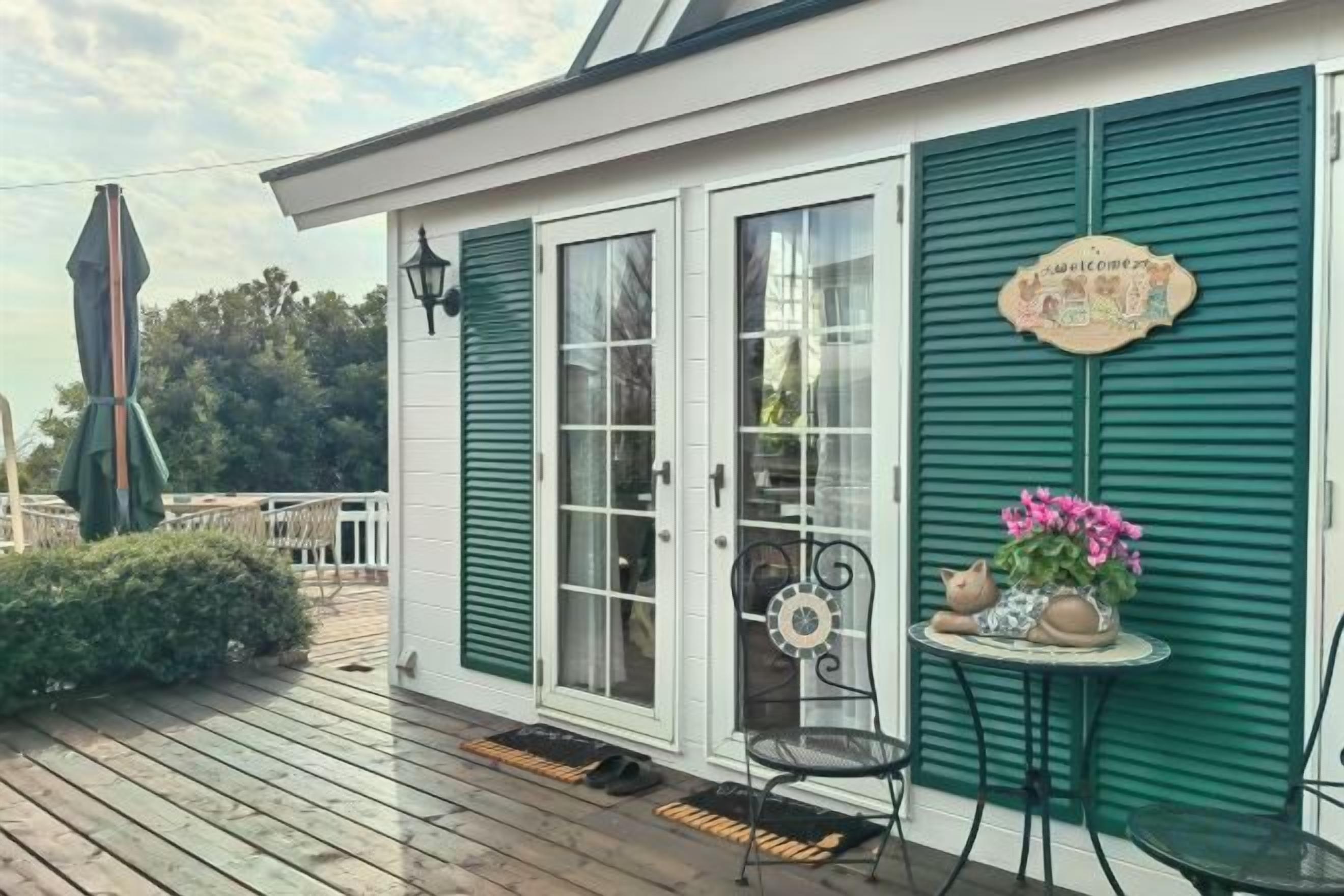 Una terraza de madera con un área de estar cubierta, una puerta con paneles de vidrio y un letrero decorativo.