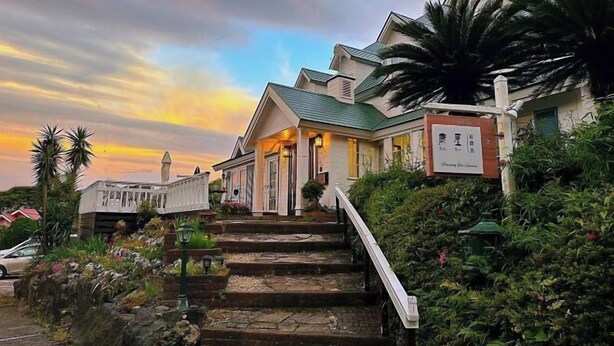 A two-story house with a staircase leading to the entrance, surrounded by lush greenery and a sunset sky. - TangWu (Ito)