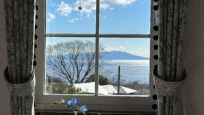 A window with a view of a mountain and a body of water, curtains with a pattern, and a hanging light fixture. - TangWu (Ito)