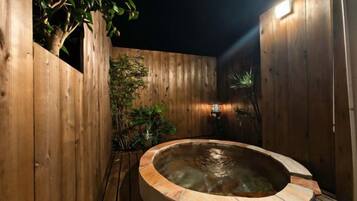 Área externa cercada por madeira, com hidromassagem, deck de madeira e plantas em vasos.