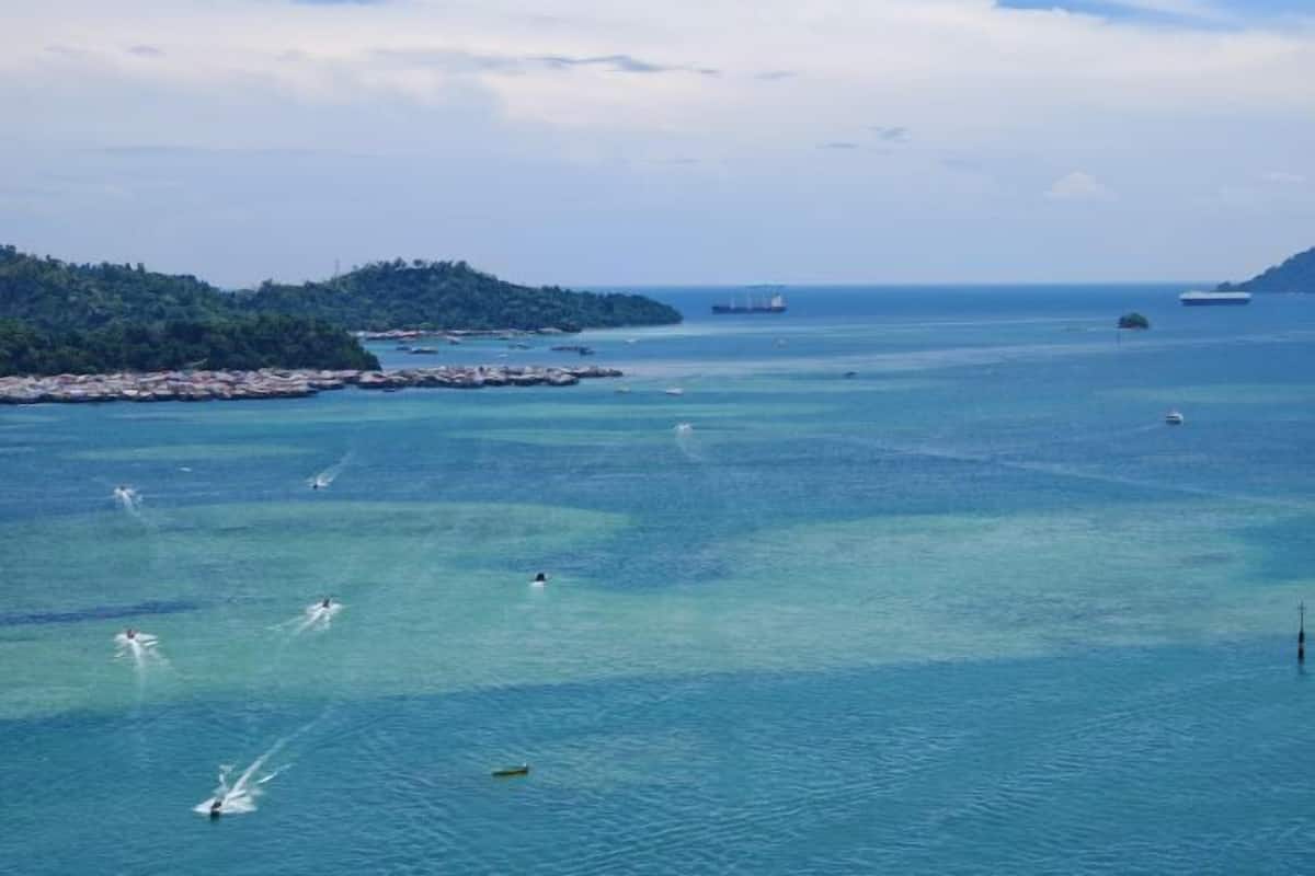 A coastal view with clear blue waters, boats, and a distant island.