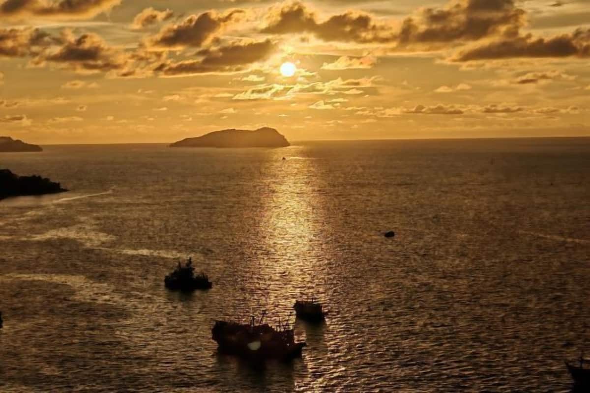 Solnedgang over et roligt hav med en fjernd island og et par både.
