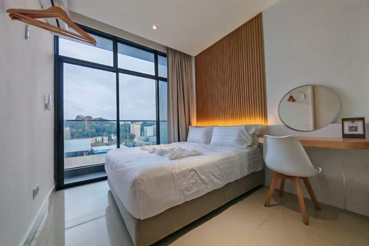 A modern bedroom with a large window, a bed, a desk, and a chair.