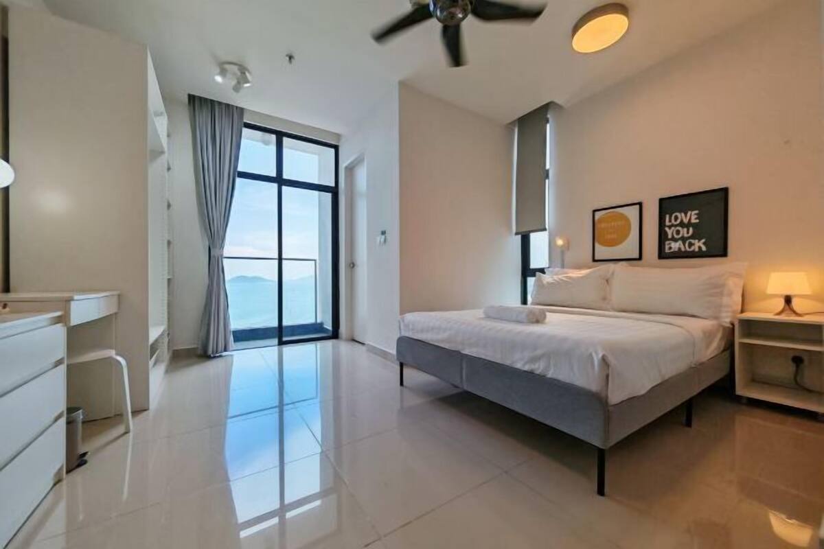 A modern bedroom with a large bed, a ceiling fan, a nightstand, and a view through a glass door.