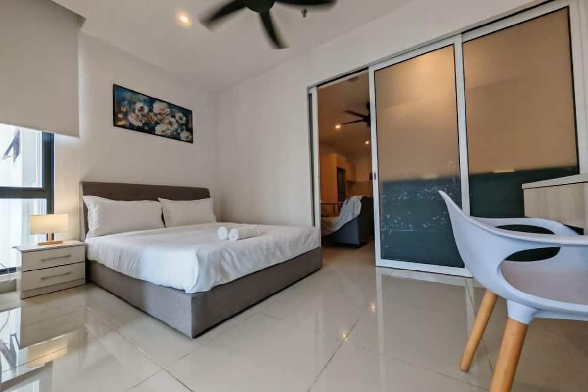 A modern bedroom with a bed, a nightstand, a chair, and a sliding glass door leading to a balcony.