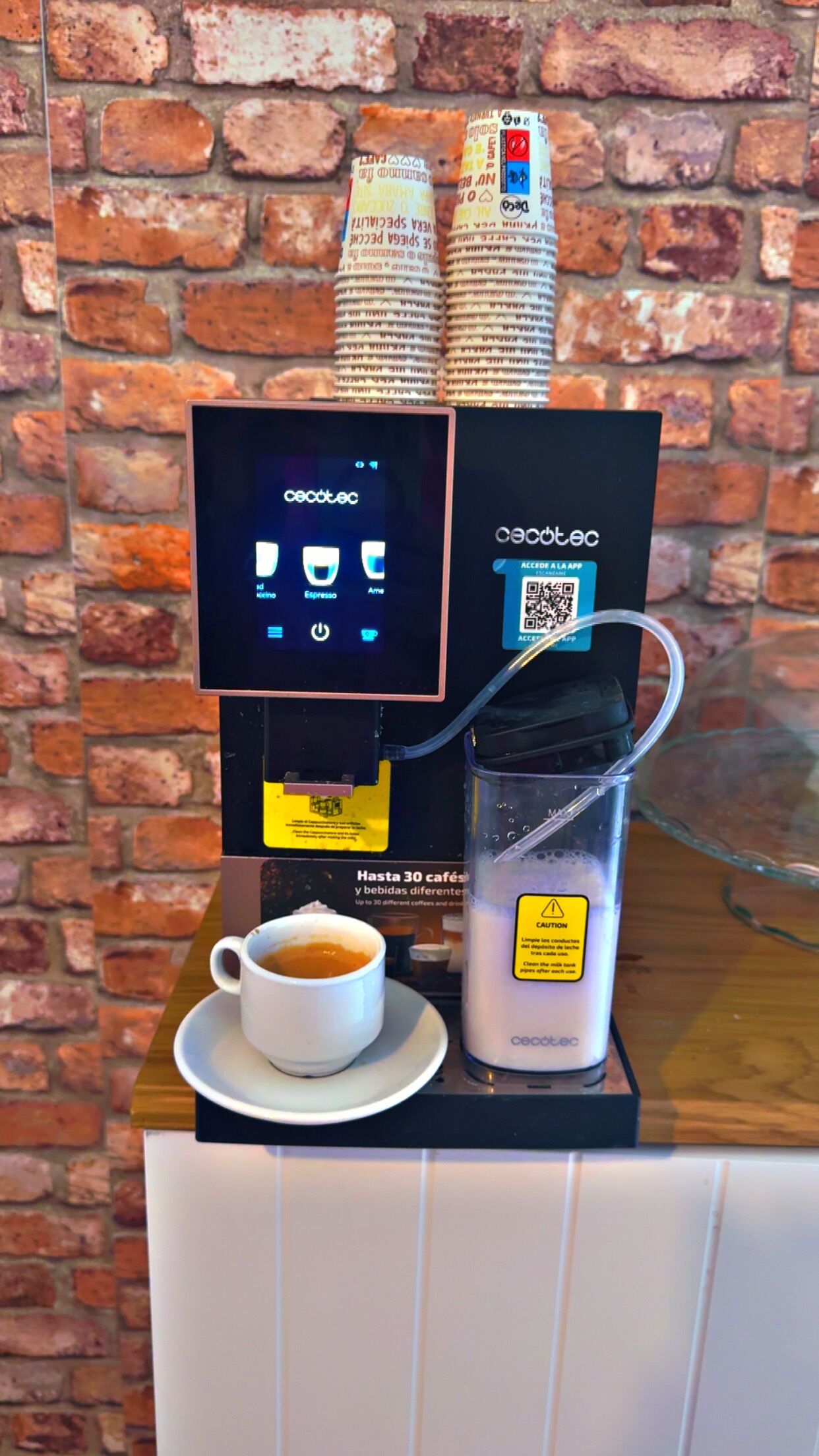 A coffee machine with a digital display, a cup of coffee, and a stack of newspapers.