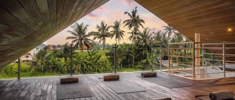 An open-air terrace with wooden flooring and a view of palm trees and greenery.