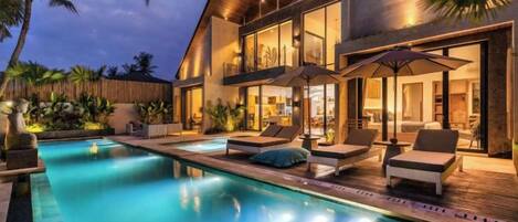 A modern house with a swimming pool, outdoor seating, and a well-lit interior.