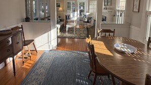 A spacious dining area with a wooden table and chairs, a blue patterned rug, and a view into a living room with a sofa and a dining table. - 418 E. Third In Lakeside (Lakeside)