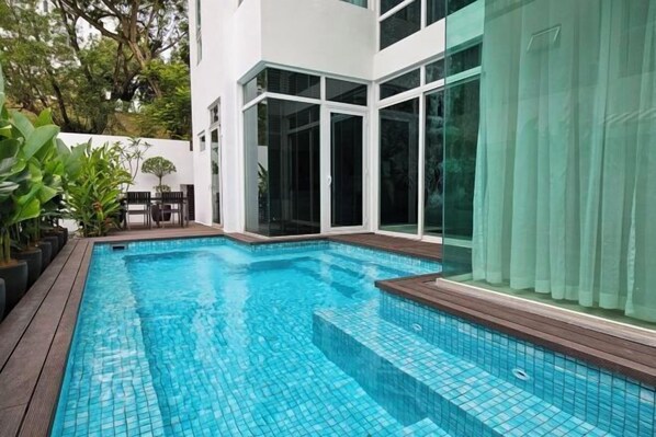 A modern outdoor swimming pool with clear blue tiles, surrounded by a wooden deck and potted plants. - Villa Homescape, Mont Kiara (Kuala Lumpur)