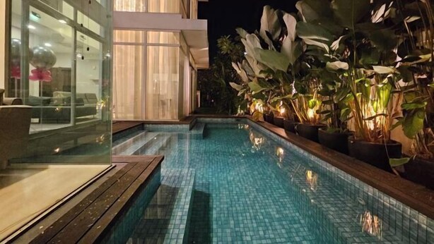A swimming pool with tiled flooring, surrounded by potted plants and a modern building with large windows. - Villa Homescape, Mont Kiara (Kuala Lumpur)