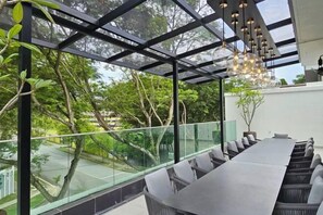 A modern conference room with a long table and chairs, large windows with a view of trees and a road, and a hanging light fixture. - Villa Homescape, Mont Kiara (Kuala Lumpur)
