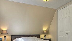 A bedroom with a bed, two bedside tables with lamps, a ceiling light, and a door.