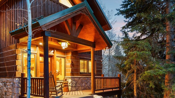 A log cabin with a porch, stone foundation, and a wooden deck. - Escape Lodge - Hot Tub, Large Deck, Sauna, Gym. (Sundance)