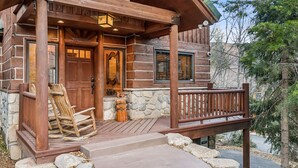 A log cabin with a wooden porch, stone foundation, and a wooden door. - Escape Lodge - Hot Tub, Large Deck, Sauna, Gym. (Sundance)
