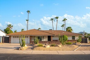 A single-story house with a brick facade, a garage, and a front yard with cacti and palm trees. - Sun-Kissed in the Desert!  Heated Private Pool, Family-Friendly, Near Golf & Hiking (Phoenix)