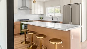 Una cocina moderna con una isla grande, taburetes de bar, un refrigerador de acero inoxidable y una ventana con persianas.