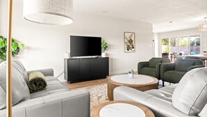 Una sala de estar moderna con un sofá, sillones, una mesa de centro, un televisor sobre un mueble negro y una planta.