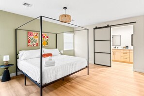 A modern bedroom with a four-poster bed, a bedside table with a lamp, and a large window with blinds. - Sun-Kissed in the Desert!  Heated Private Pool, Family-Friendly, Near Golf & Hiking (Phoenix)