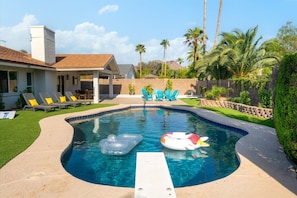 A swimming pool with inflatable toys, a covered patio with chairs, and a house in the background. - Sun-Kissed in the Desert!  Heated Private Pool, Family-Friendly, Near Golf & Hiking (Phoenix)