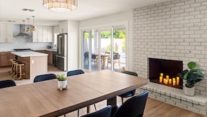 Una cocina moderna con una isla central, una zona de comedor con una mesa de madera y una chimenea con velas.