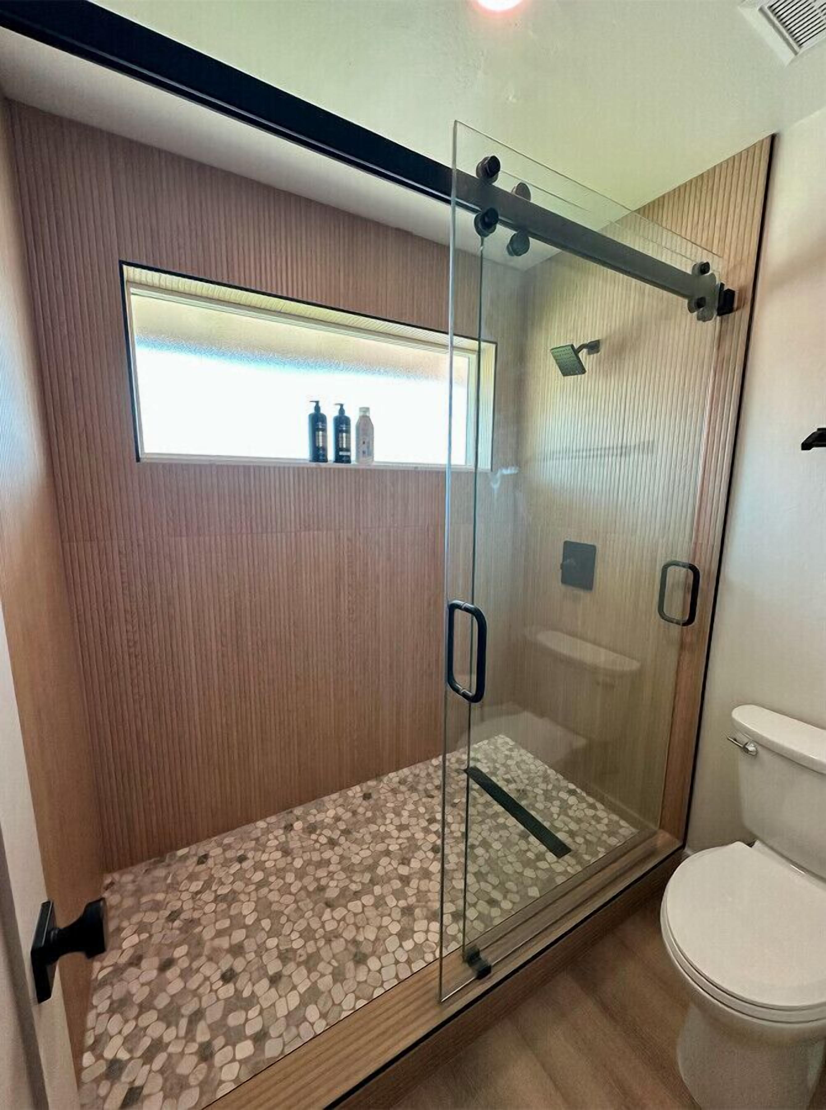 A modern bathroom with a glass-enclosed shower, a wooden vanity, and a toilet.