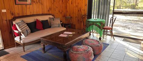 A wooden interior with a sofa, a coffee table, and a view through a window.