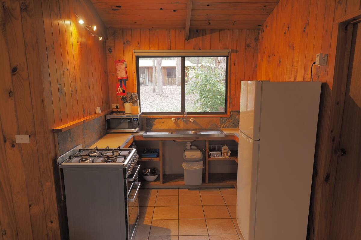 A compact kitchen with wooden walls, a gas stove, a microwave, a sink, and a refrigerator.