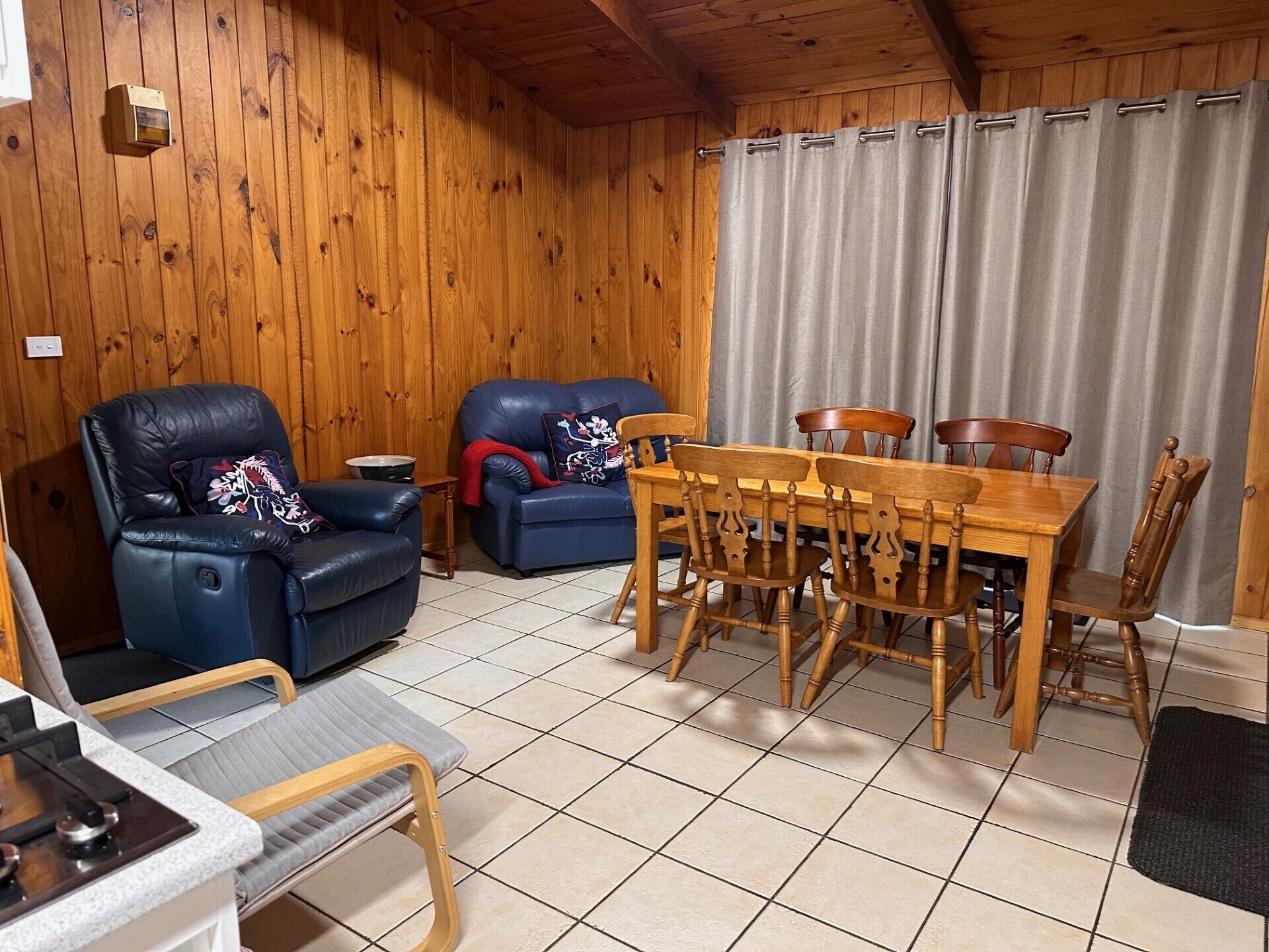 A cozy room with wooden walls, a dining table with chairs, a sofa, and a small kitchen area.