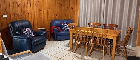 A cozy room with wooden walls, a dining table with chairs, a sofa, and a small kitchen area.