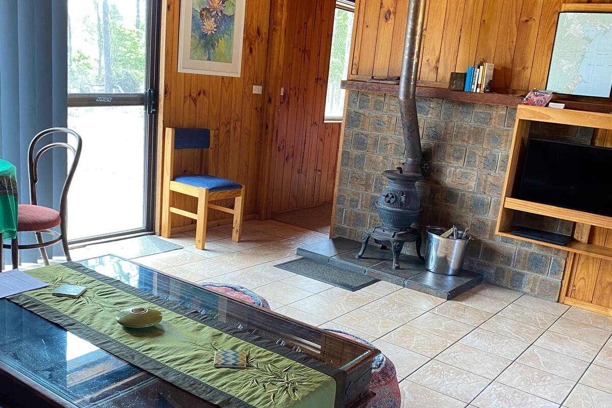 A wooden interior with a glass-top dining table, a stone fireplace, and a television on a wooden stand.