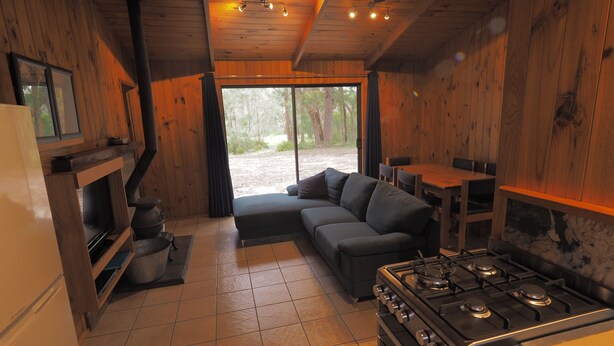 A cozy cabin interior with a kitchen, a sofa, and a dining table. - Woodbine Park Eco Cabins (Bournda)