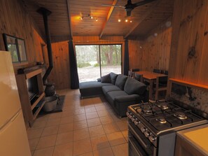 A cozy cabin interior with a kitchen, a sofa, and a dining table. - Woodbine Park Eco Cabins (Bournda)
