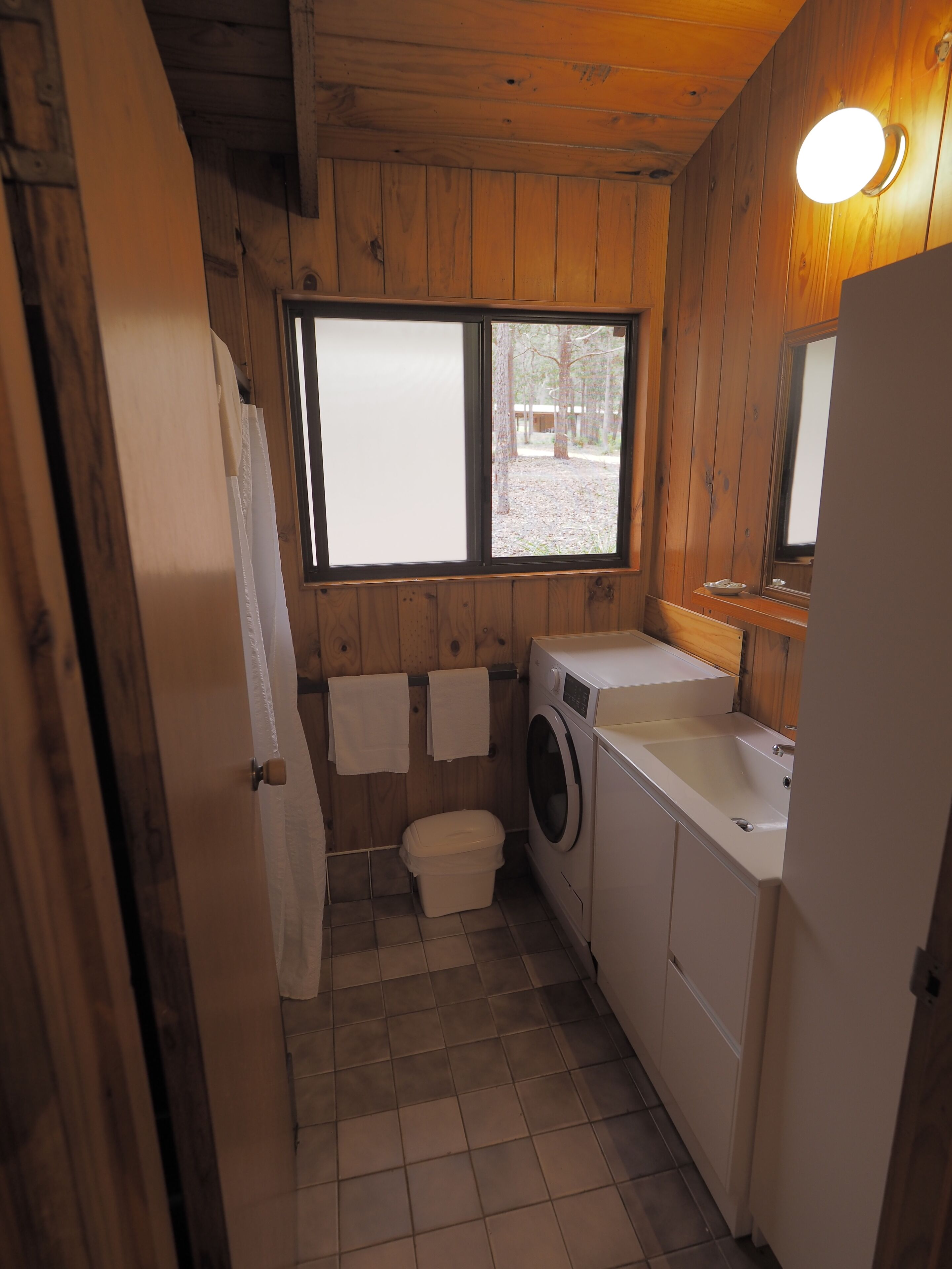 A small, compact bathroom with wooden walls, a washing machine, a toilet, and a sink.