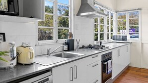 Une cuisine moderne avec des meubles blancs, des appareils en acier inoxydable et de grandes fenêtres offrant une vue sur les arbres.