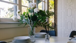 Una mesa de comedor preparada con platos, cubiertos y un centro de mesa de flores blancas y follaje verde.