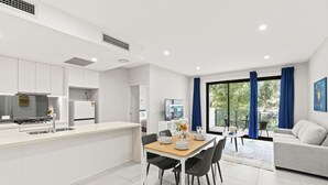 A modern kitchen with white cabinets, a built-in stove, and a dining area with a wooden table and chairs.
