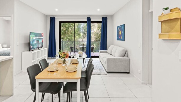 A modern living room with a dining area, a sofa, a TV, and a balcony with curtains.