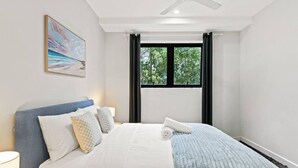 A bedroom with a bed, a ceiling fan, a window with curtains, and a painting on the wall.