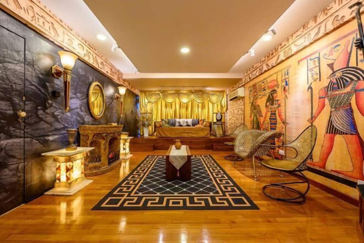 A room with a stone wall, a fireplace, a bed with golden curtains, and Egyptian-themed artwork.