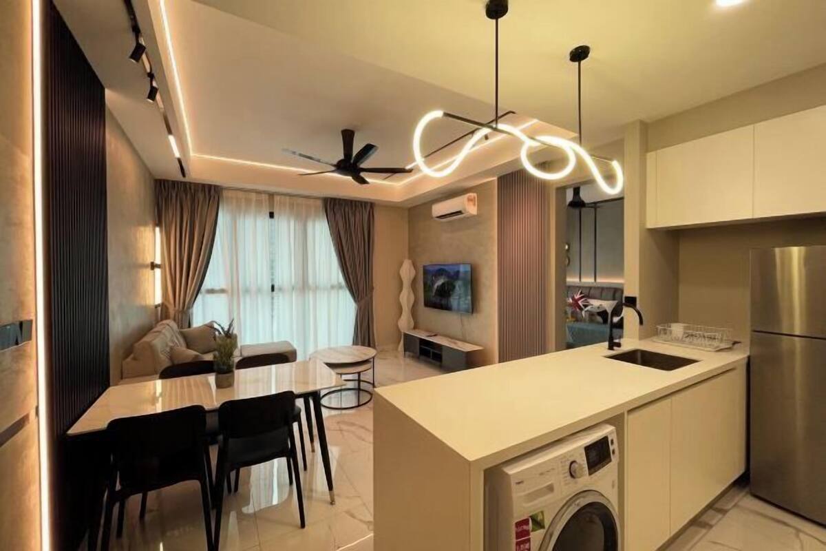 Une cuisine moderne équipée d’un lave-linge intégré, un coin repas avec une table et des chaises, et un espace de vie comprenant un canapé et un téléviseur.
