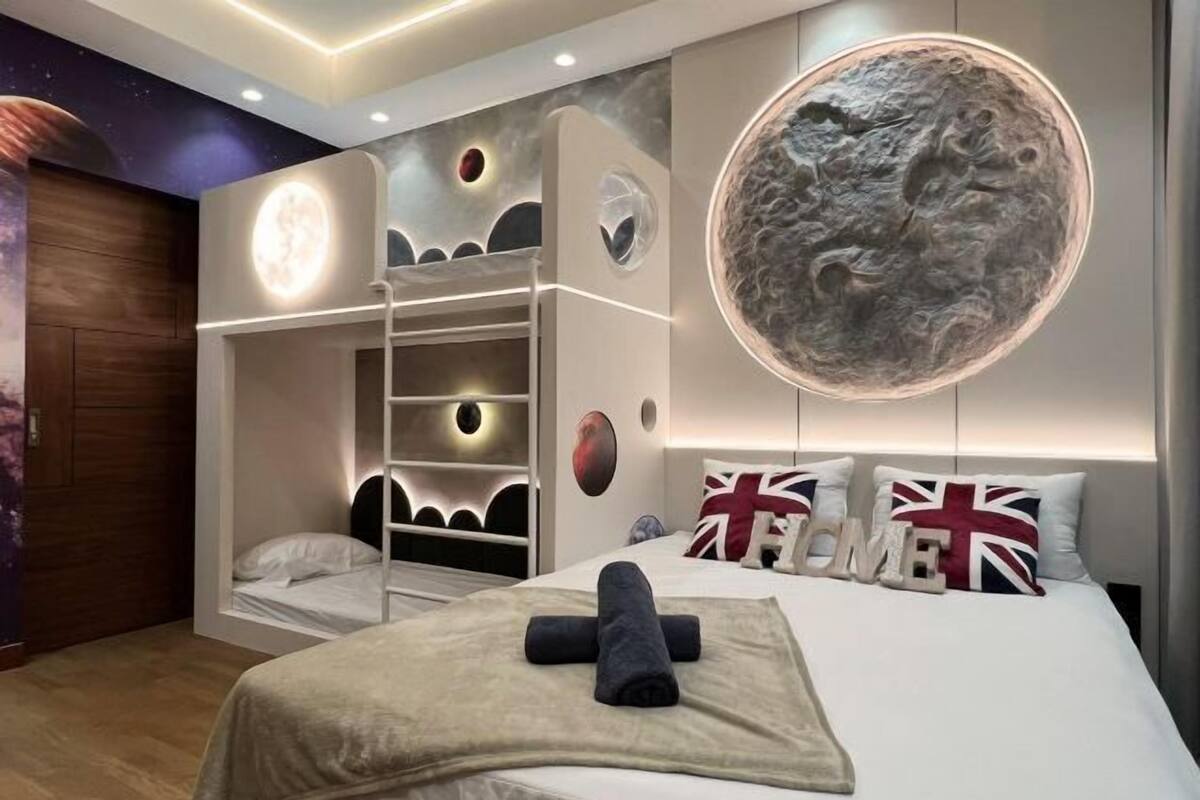 Une chambre avec un lit superposé, une grande fresque murale représentant une lune et un lit orné d’oreillers aux couleurs de l’Union Jack.